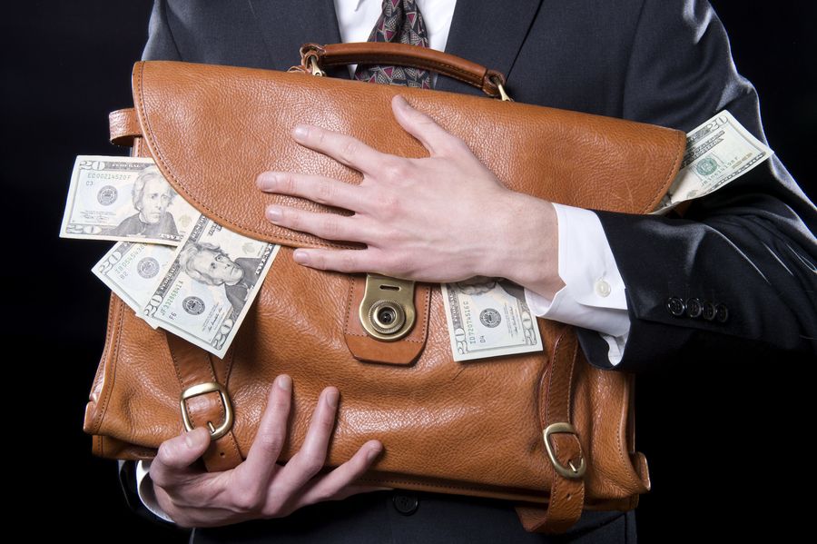 Closeup of man holding briefcase with money spilling out close to his chest